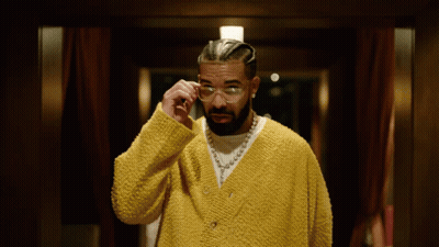 A Man Wearing A Yellow Sweater And Glasses Looks Down GIF