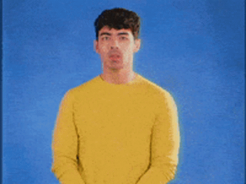 A Man Wearing A Yellow Sweater Stands In Front Of A Blue Background GIF