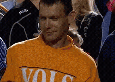 A Man Wearing A Yellow Sweater With The Word Volc On It Is Standing In A Crowd Of People . GIF