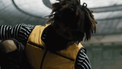 A Man Wearing A Yellow Vest And A Striped Shirt Is Standing On A Skateboard . GIF