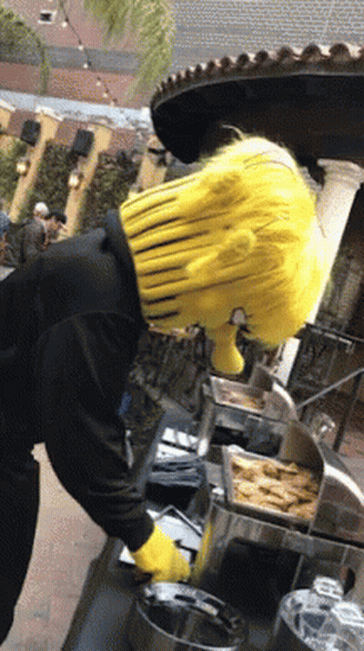A Man Wearing A Yellow Wig And Yellow Gloves Is Standing In Front Of A Buffet Line GIF