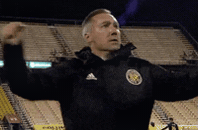 A Man Wearing An Adidas Jacket Is Standing In A Stadium With His Arms Outstretched . GIF