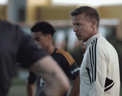 A Man Wearing An Adidas Jacket Stands In Front Of A Group Of Men GIF