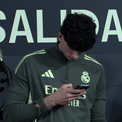 A Man Wearing An Adidas Shirt Looks At His Cell Phone GIF