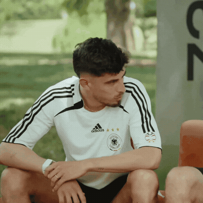 A Man Wearing An Adidas Shirt Sits On A Chair GIF
