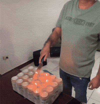 A Man Wearing An Aeropostale Shirt Is Cutting A Bunch Of Candles With A Knife GIF