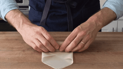 A Man Wearing An Apron Is Folding A Piece Of Paper GIF