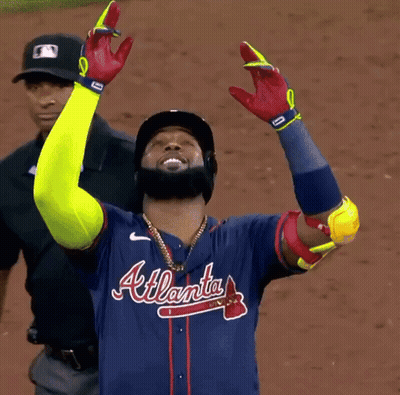 A Man Wearing An Atlanta Baseball Jersey Holds His Arms Up In The Air GIF