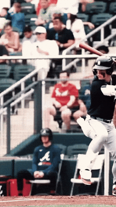 A Man Wearing An Atlanta Shirt Sits In The Dugout Watching A Baseball Player Swing His Bat GIF