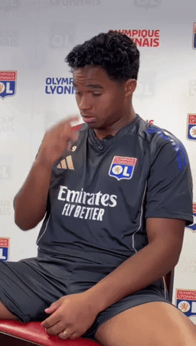 A Man Wearing An Emirates Fly Better Jersey Sits On A Red Chair GIF
