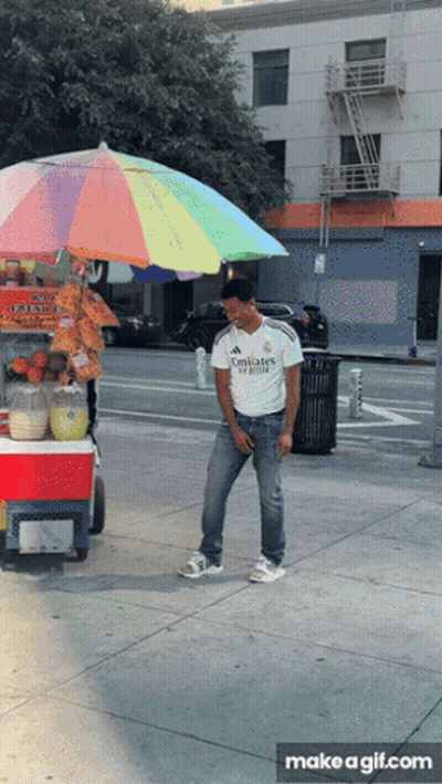 A Man Wearing An Emirates Shirt Is Standing In Front Of A Cart GIF