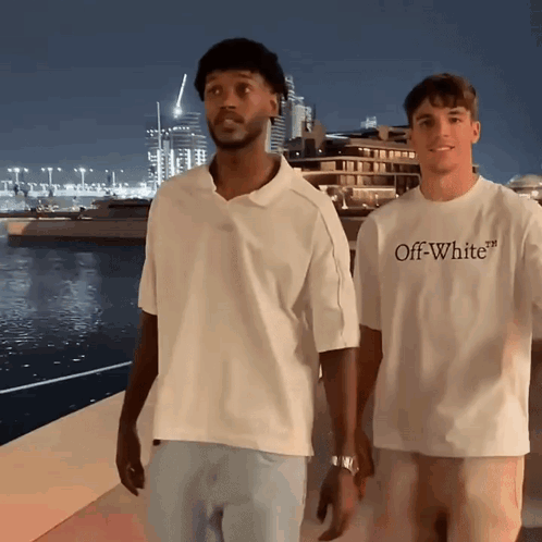 A Man Wearing An Off White T-Shirt Is Standing Next To Another Man GIF