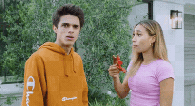 A Man Wearing An Orange Champion Hoodie Is Standing Next To A Woman In A Pink Shirt GIF