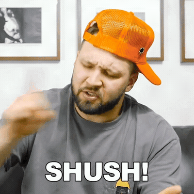 A Man Wearing An Orange Hat And A Grey Shirt Says " Shush " GIF
