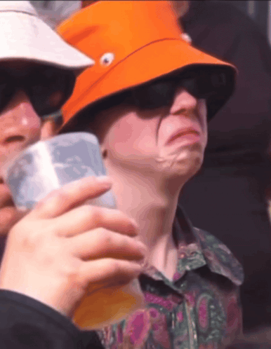 A Man Wearing An Orange Hat Is Holding A Cup Of Beer GIF