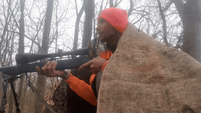 A Man Wearing An Orange Hat Is Holding A Rifle GIF