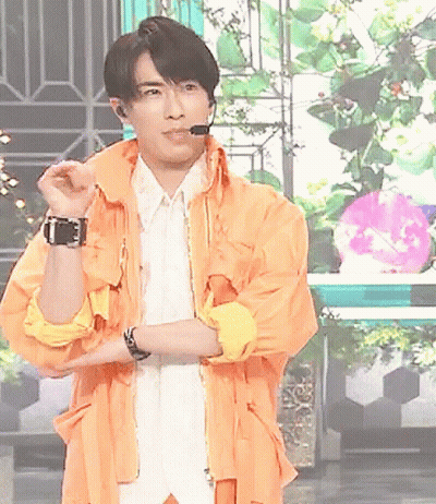 A Man Wearing An Orange Jacket And A White Shirt Is Standing With His Arms Crossed GIF