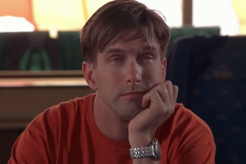 A Man Wearing An Orange Shirt And A Silver Watch Rests His Chin On His Hand GIF