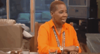 A Man Wearing An Orange Shirt Is Sitting At A Table With A Glass Of Water . GIF
