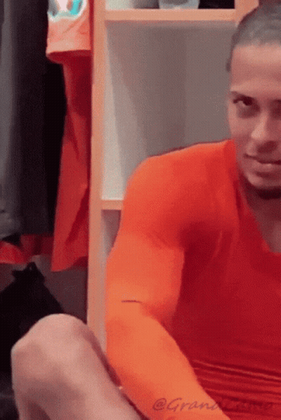 A Man Wearing An Orange Shirt Is Sitting In A Locker Room GIF