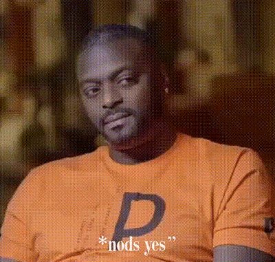 A Man Wearing An Orange Shirt With The Letter D On It Is Sitting Down . GIF