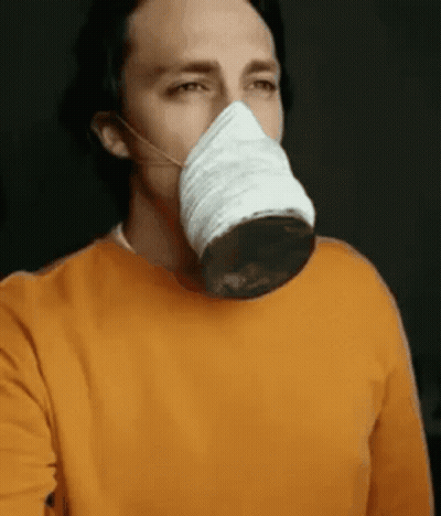 A Man Wearing An Orange Sweater Is Wearing A Mask On His Face . GIF