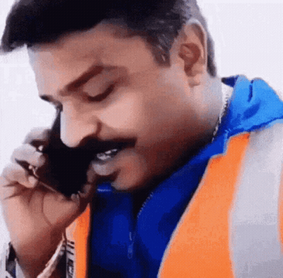 A Man Wearing An Orange Vest Is Talking On A Cell Phone . GIF