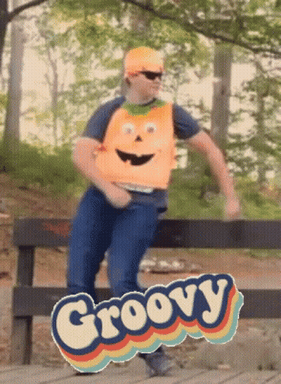 A Man Wearing An Orange Vest With A Face On It Is Dancing In Front Of A Groovy Sign GIF