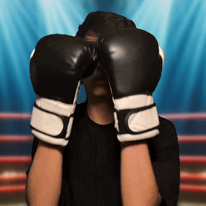 A Man Wearing Black And White Boxing Gloves Covers His Face GIF