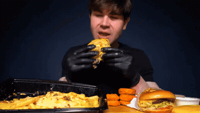 A Man Wearing Black Gloves Eats A Cheeseburger GIF