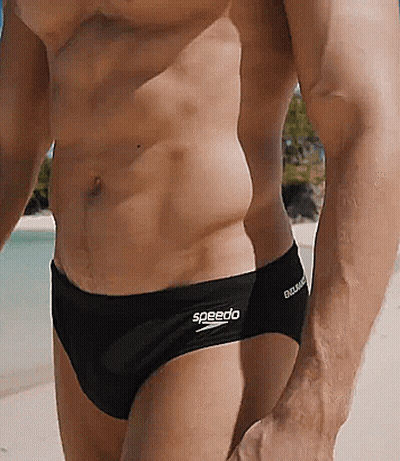 A Man Wearing Black Speedo Swim Briefs Is Standing On A Beach GIF