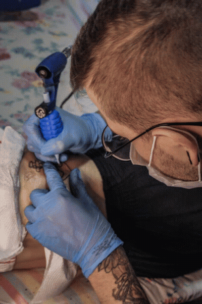 A Man Wearing Blue Gloves Is Getting A Tattoo On Someone 'S Leg GIF
