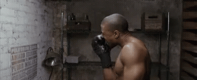 A Man Wearing Boxing Gloves Is Drinking Water From A Bottle In A Room . GIF