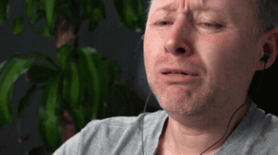 A Man Wearing Ear Buds And A Gray Shirt Is Crying GIF