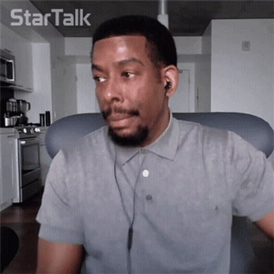 A Man Wearing Ear Buds And A Grey Shirt Is Sitting In Front Of A Star Talk Logo GIF
