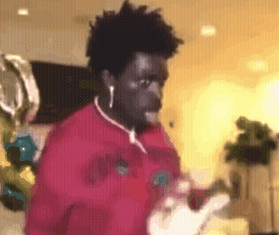 A Man Wearing Ear Buds And A Red Shirt Is Standing In A Room . GIF