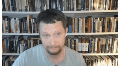 A Man Wearing Ear Buds Is Standing In Front Of A Bookshelf GIF