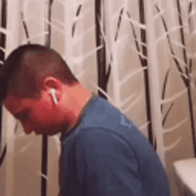 A Man Wearing Ear Buds Is Standing In Front Of A Wall With Trees Painted On It . GIF