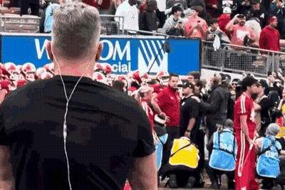 A Man Wearing Ear Buds Stands In Front Of A Sign That Says Wom Social GIF