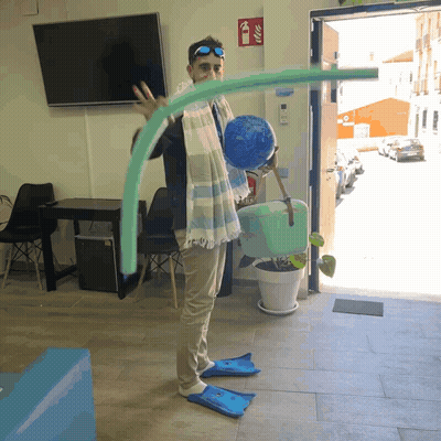 A Man Wearing Flippers Is Holding A Swimming Noodle In Front Of A Fire Extinguisher GIF