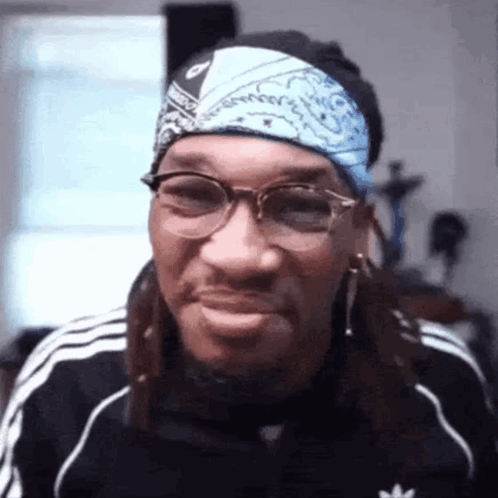 A Man Wearing Glasses And A Bandana Is Smiling And Making A Funny Face . GIF