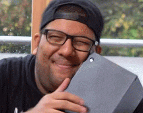 A Man Wearing Glasses And A Baseball Cap Is Smiling While Holding A Tablet . GIF