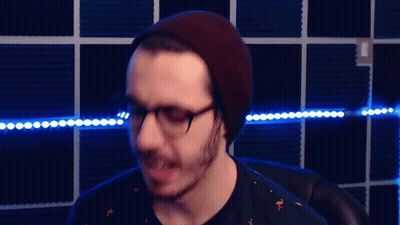 A Man Wearing Glasses And A Beanie Is Standing In Front Of Blue Lights GIF