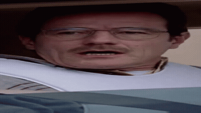 A Man Wearing Glasses And A Bib On His Neck Looks At The Camera GIF
