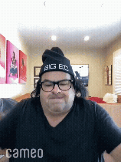 A Man Wearing Glasses And A Big Eq Hat Is Making A Funny Face . GIF