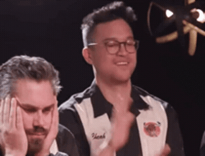 A Man Wearing Glasses And A Black And White Shirt Is Clapping His Hands . GIF