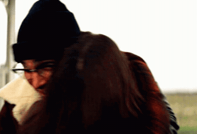 A Man Wearing Glasses And A Black Beanie Holds A Woman In His Arms GIF