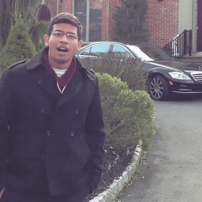 a man wearing glasses and a black coat stands in front of a black car