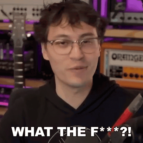 A Man Wearing Glasses And A Black Hoodie Is Holding A Guitar And Says What The F *** ? GIF