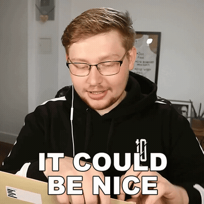 A Man Wearing Glasses And A Black Hoodie Is Holding A Piece Of Paper That Says It Could Be Nice GIF